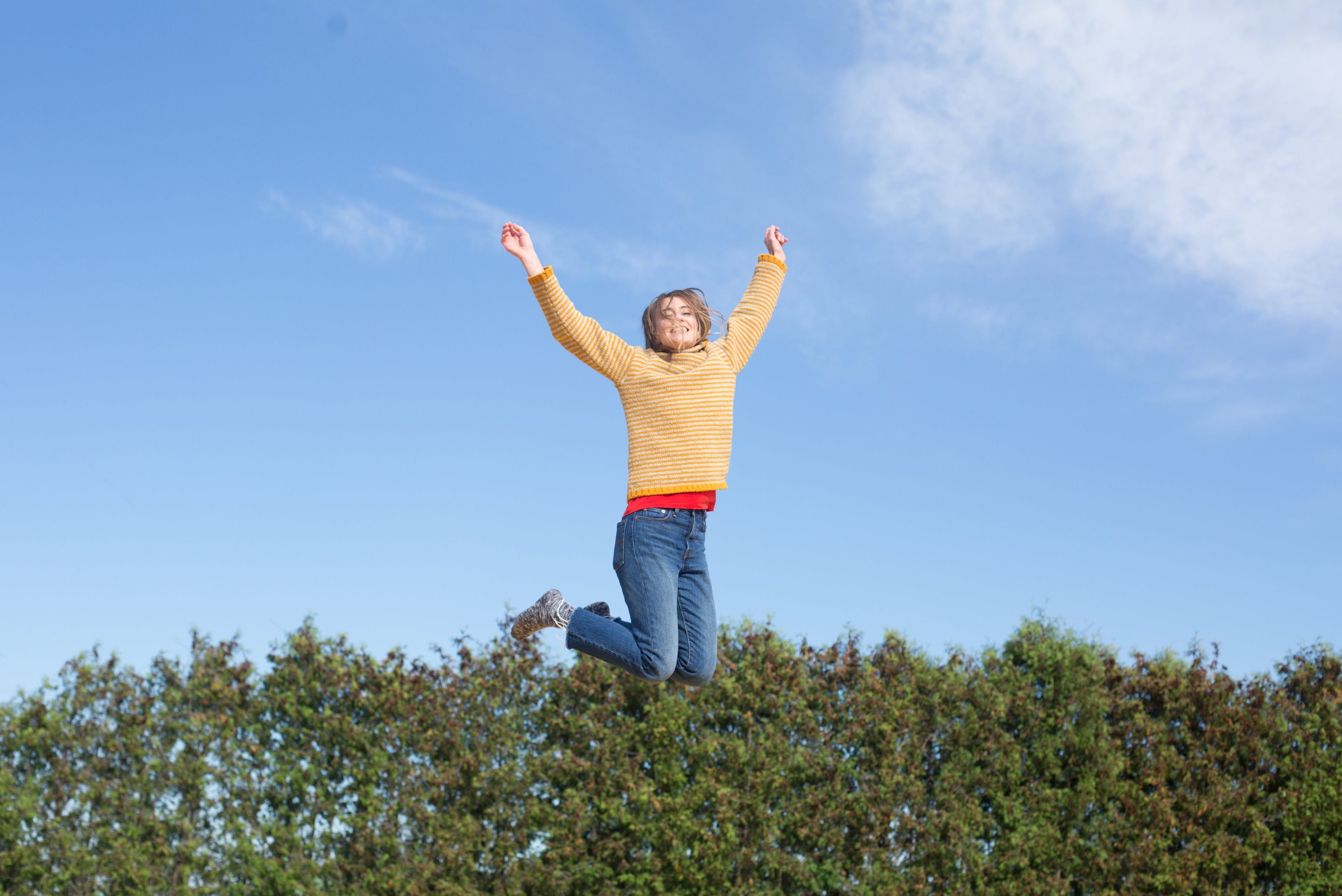 Person standing on a sand dune with arms raised against a blue sky